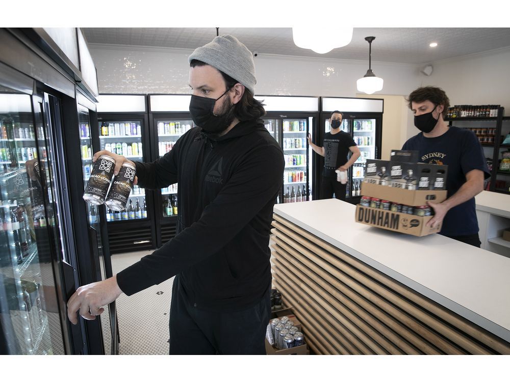 MONTREAL, QUE.: APRIL 23, 2021 — Kevin Demers stocks one of the beer fridges at Dépanneur Bière Froide Cold Beer during the COVID-19 pandemic. With Demers are co-owners Sam Kirk, far right, and Fred Masse, in background.